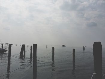 Wooden posts in sea against sky