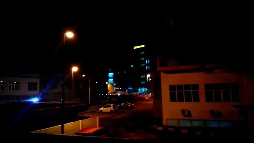 Illuminated street by buildings in city at night