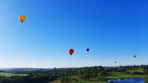 Hot air balloons flying over landscape against clear blue sky