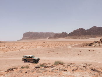 Off-road vehicle on desert against clear sky