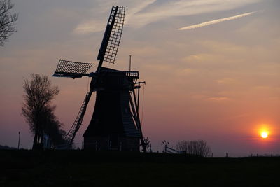 Traditional windmill on field against sky at sunset