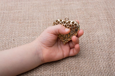 Cropped hand holding heart shape toy on burlap