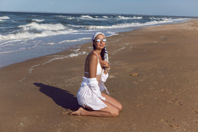 Woman in a white bathing suit and hat sunglasses on an empty sandy beach