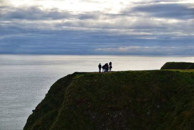 People standing on cliff by sea against cloudy sky