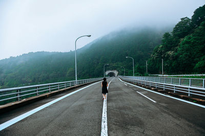 Rear view of woman walking on bridge by mountain during foggy weather
