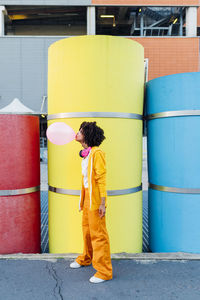 Woman blowing bubblegum in front of multi colored pipes