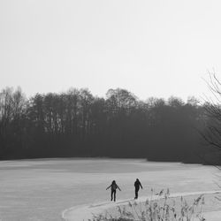 Friends ice skating on snowy field against clear sky during winter