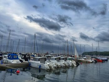 Boats in harbor against cloudy sky