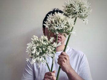 Man holding 3 stalks of white, african lilies flowers against white background.