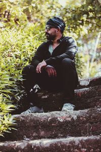 Young man looking down while sitting on plant