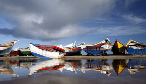 Fishing boats on beach against cloudy sky