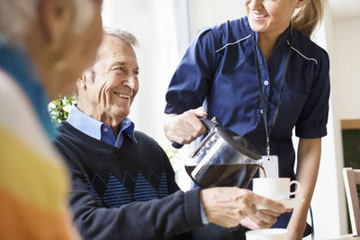Midsection of happy female caretaker serving black coffee to senior man at nursing home