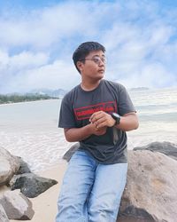 Young man standing on rock against sky