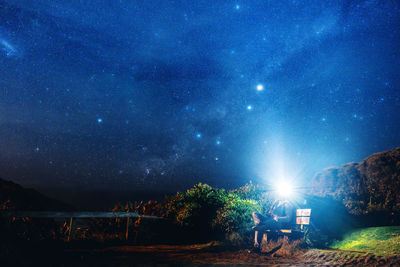 People sitting by illuminated lights against sky at night