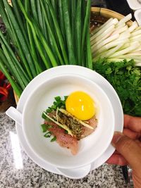 Cropped image of hand holding egg and meat in plate in kitchen