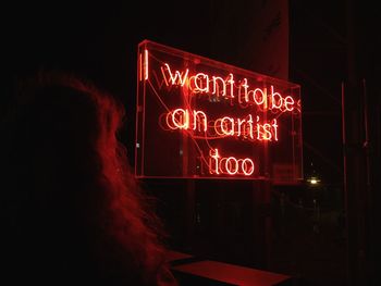 Rear view of woman looking at illuminated information sign during night