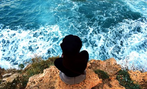 High angle view of woman sitting on cliff by sea