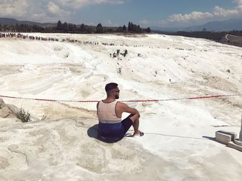 Rear view of man sitting on white rocks against sky