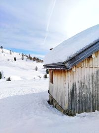 Snow covered field against sky with wooden hut