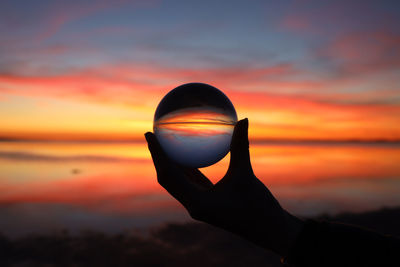 Silhouette person holding crystal ball during sunset