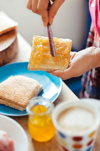 Cropped image of woman spreading orange jam on bread at home