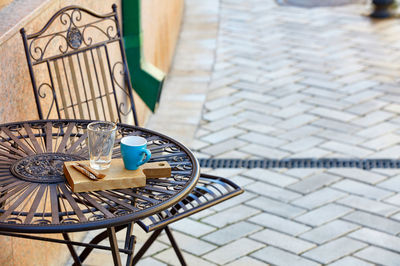 Stylish outdoor metal table with a turquoise cup, a transparent glass on a wooden stand.