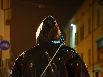 Rear view of person wearing black raincoat during rainy season at night