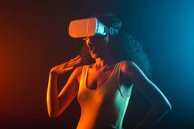 Woman standing by illuminated light against orange wall