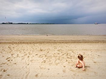 Woman sitting on beach against sky