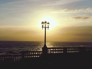 Silhouette street light by sea against sky during sunset