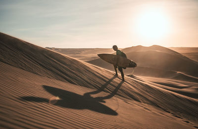 Man on sand dune in desert against sky