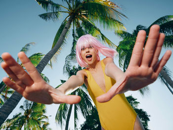 Portrait of young woman with arms raised standing against sky