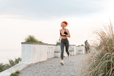Full length of young woman walking on footpath against clear sky