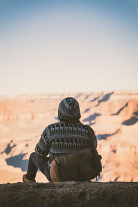 Rear view of man sitting on desert against sky