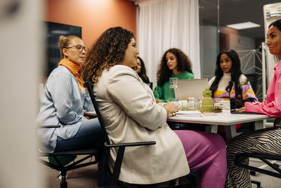 Side view of female entrepreneur sitting with colleagues during business meeting at office