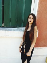 Portrait of young woman standing against wall