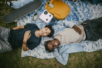 Directly above portrait of happy teenage boy lying down with male friend on picnic blanket