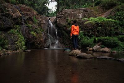 Rear view of man standing on rock against waterfall