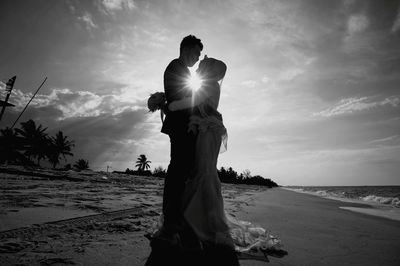 Side view of couple embracing while standing on shore at beach