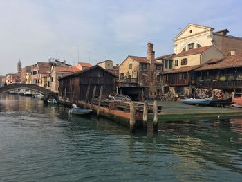 Boats moored in canal by buildings in city against sky