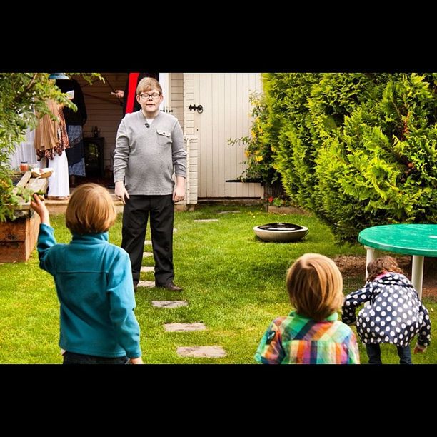 rear view, lifestyles, leisure activity, childhood, casual clothing, grass, togetherness, full length, girls, transfer print, park - man made space, boys, green color, tree, men, sitting, bonding, elementary age