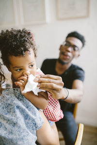 Young man wiping mouth of daughter being held by woman at home