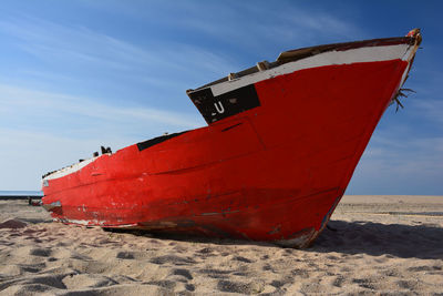Red boat moored on beach against sky