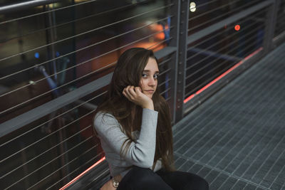 Portrait of young woman sitting on footbridge against railing