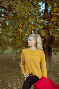 Woman looking away while standing by tree during autumn