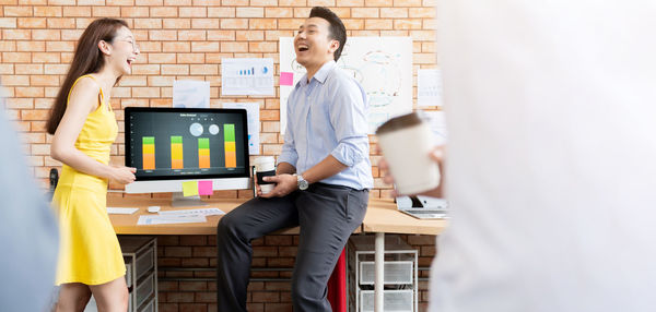 Cheerful colleagues laughing while working at desk in office