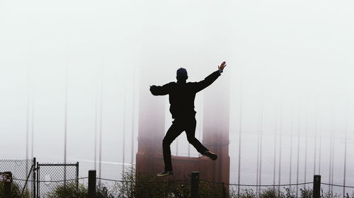 Full length rear view of man jumping in city during foggy weather