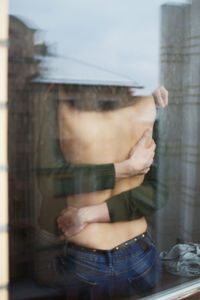 Midsection of topless woman embracing man seen through glass window