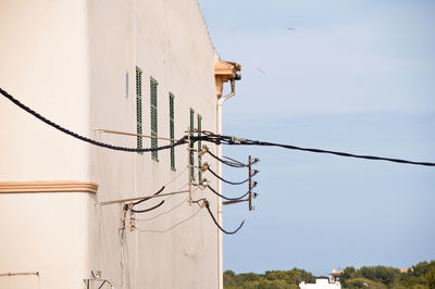 Low angle view of telephone pole by building against sky