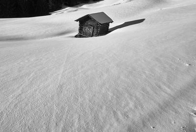 Weathered wooden hut by snow covered field in the afternoon sun